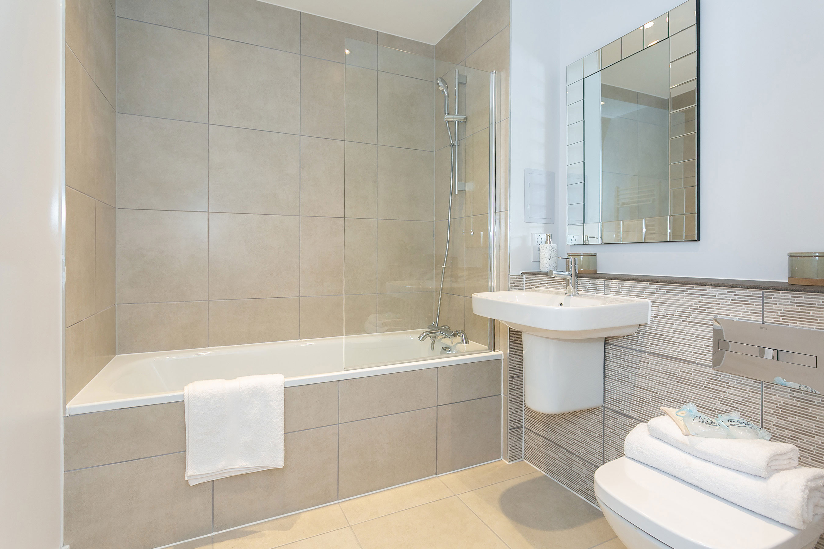 Modern bathroom with beige tiles and white ceramic goods.